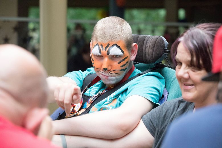 Ben, with his face painted like a lion, points towards camera. Mum Liz sits next to him.