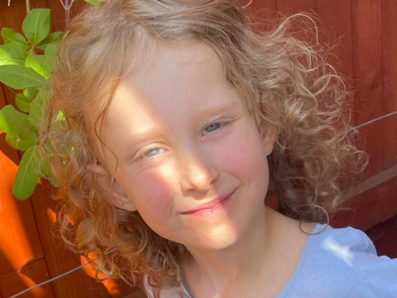 Mia, a little girl with curly blonde hair, smiles at the camera