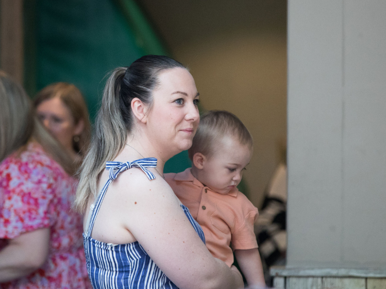 A lady with long blonde hair carries a toddler in her arms